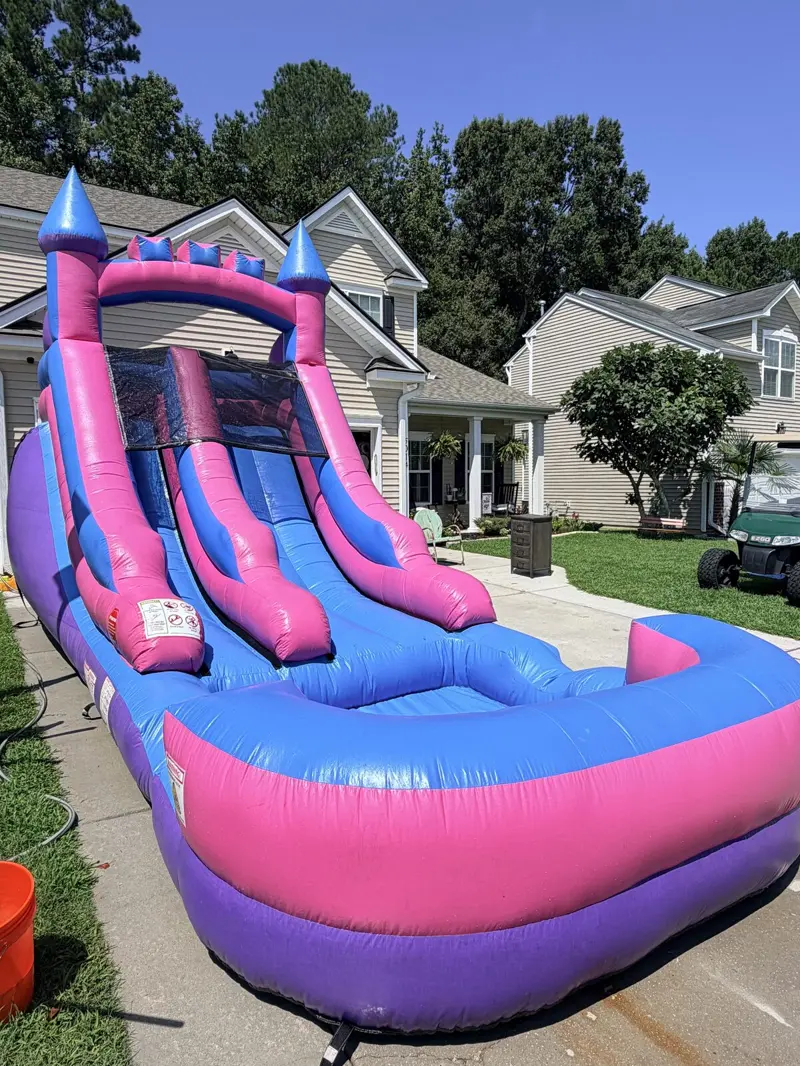 A pink and blue castle-style water slide with a splash pool, set up and ready for a party